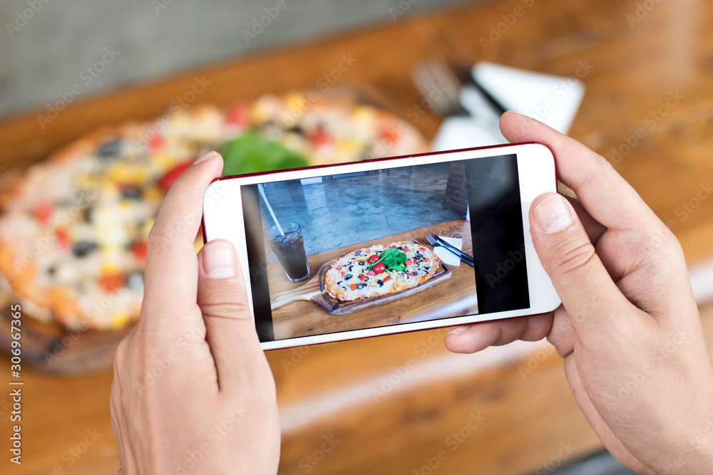 Male hand making a photo of pizza, with a mobile phone, close up, horizontal Male hand making a photo of pizza, with a mobile phone, close up, horizontal