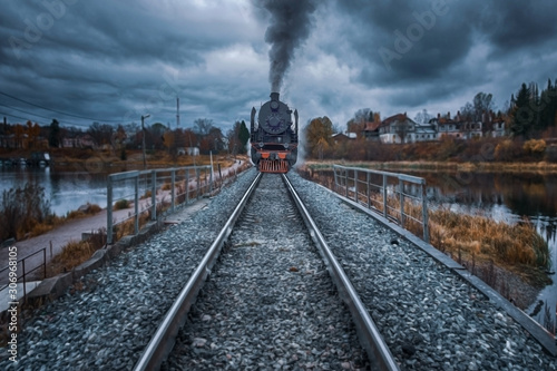 An ancient steam locomotive rides the rails of a railway on an embankment in gloomy autumn weather