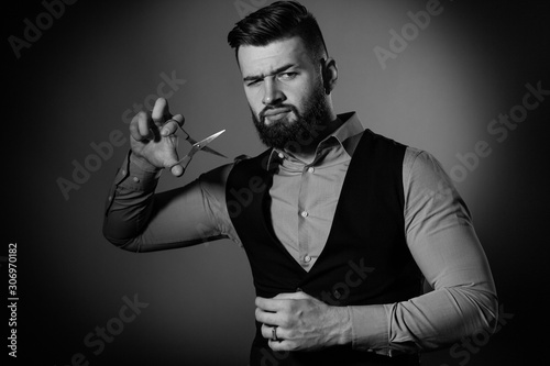 Bearded man in vest on red background. Men cut their beard with hairdressing scissors. Black and white