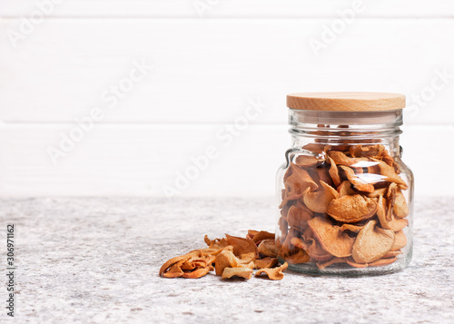 Dried apples in a glass jar with a wooden lid on a light background