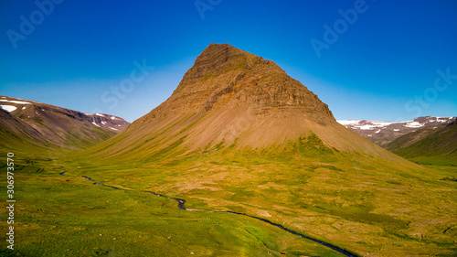 High aerial view of a stunning green valley with a river surrounded by large mountains in Westfjord. Midnight sun, Iceland