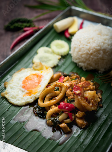 Thai food stir-fried shrimp, squid spicy and basil served with rice and fried egg on wood table