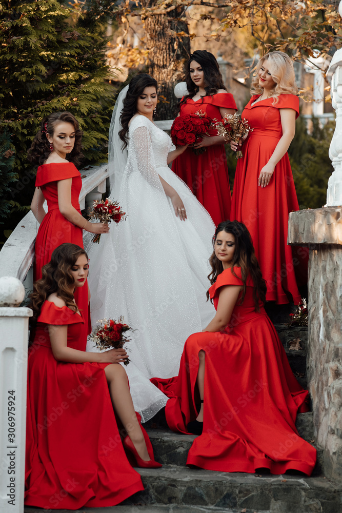 portrait of bride and bridesmaids on the stairs. Wedding in autumn. Bride in wedding dress and bridesmaids in red dresses at Stylish wedding in red color. Marriage concept. Stock-foto
