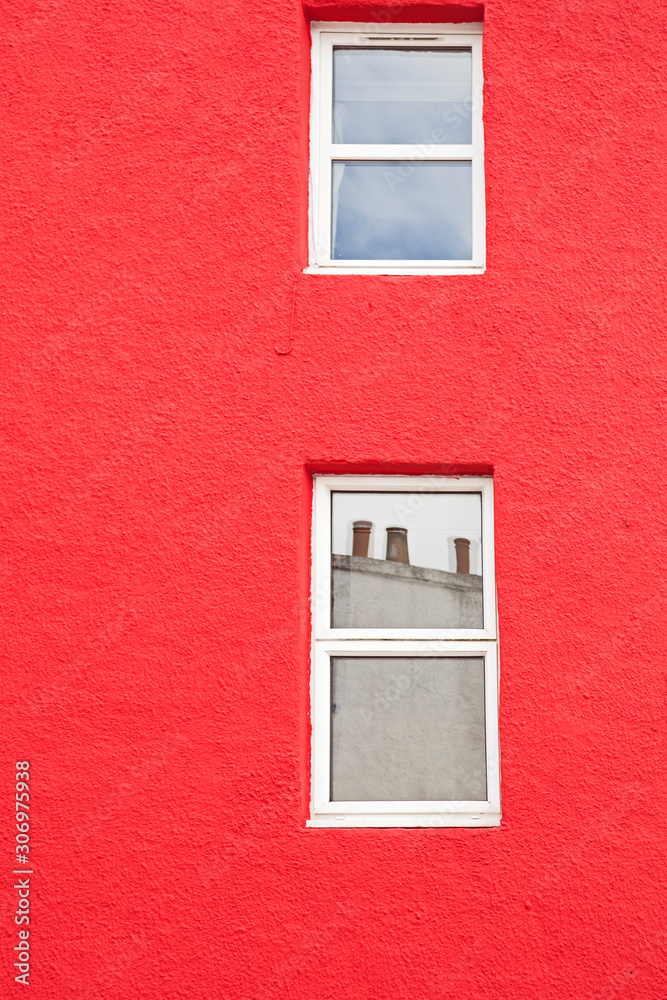 fachada pintada de rojo con dos ventanas pintadas de blanco con reflejos en los cristales