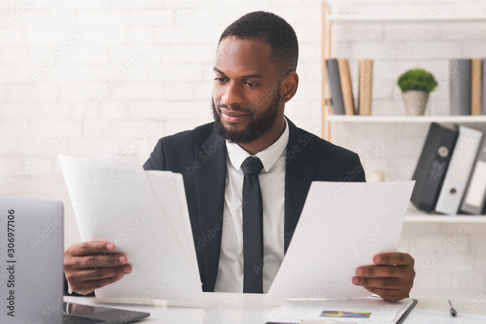 Black man in suit reading papers at his workplace