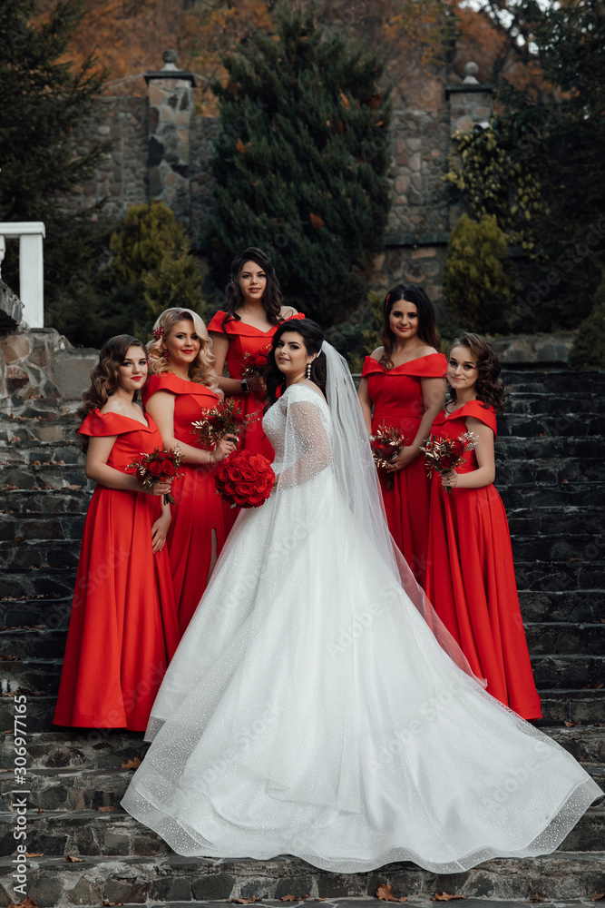 Group portrait of bride and bridesmaids on the stairs. Wedding in autumn. Bride in wedding dress and bridesmaids in red dresses at wedding day. Stylish wedding in red color. Marriage concept. Group portrait of bride and bridesmaids on the stairs. Wedding in autumn. Bride in wedding dress and bridesmaids in red dresses at wedding day. Stylish wedding in red color. Marriage concept.