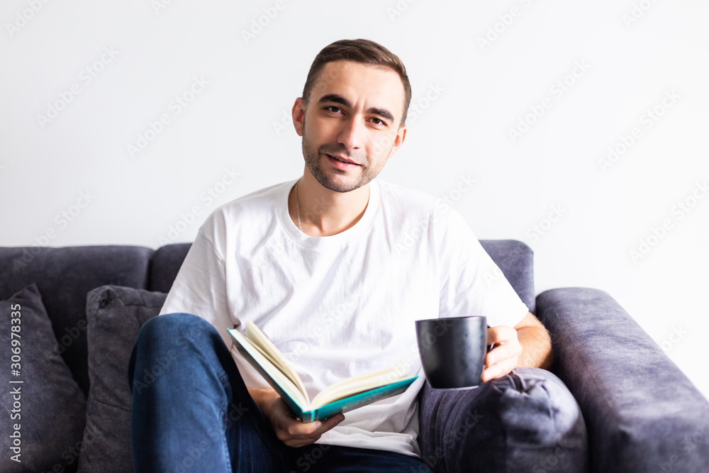 Young handsome man having coffee while reading book in living room Young handsome man having coffee while reading book in living room