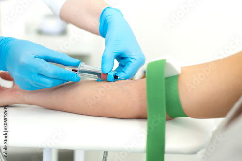 a gloved nurse inserts a needle into a vein on the patient arm and draws blood into a vacuum container. Blood sampling procedure
