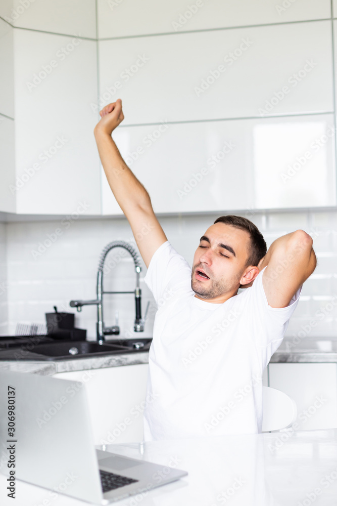 Yawning sleepy man yawn working on his laptop in kitchen in the morning. Yawning sleepy man yawn working on his laptop in kitchen in the morning.