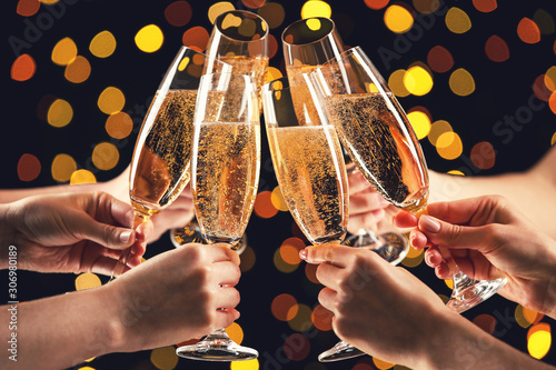 Female hands clink glasses of champagne on blurred lights background