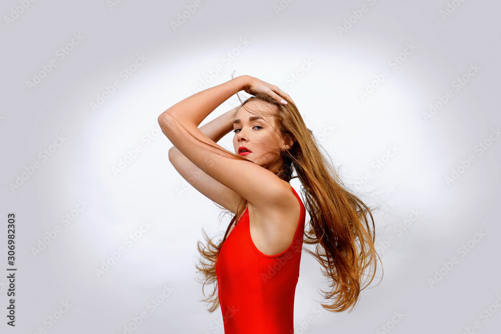 A beautiful young teenager dressed in red gets her hair blown by strong wind. She stands posing in front of a white background. A beautiful young teenager dressed in red gets her hair blown by strong wind. She stands posing in front of a white background.