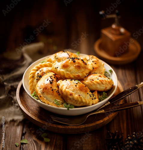 Baked dumplings (pierogi) with mushroom stuffing in a ceramic bowl on a wooden table, close-up.  Vegetarian dish