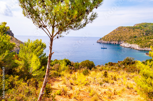 Scenic landscape view from the overgrown rocky mountains of Cilento and Vallo di Diano National Park in Campania, Italy on hidden Cala Bianca beach surrounded by rocks in Tyrrhenian sea