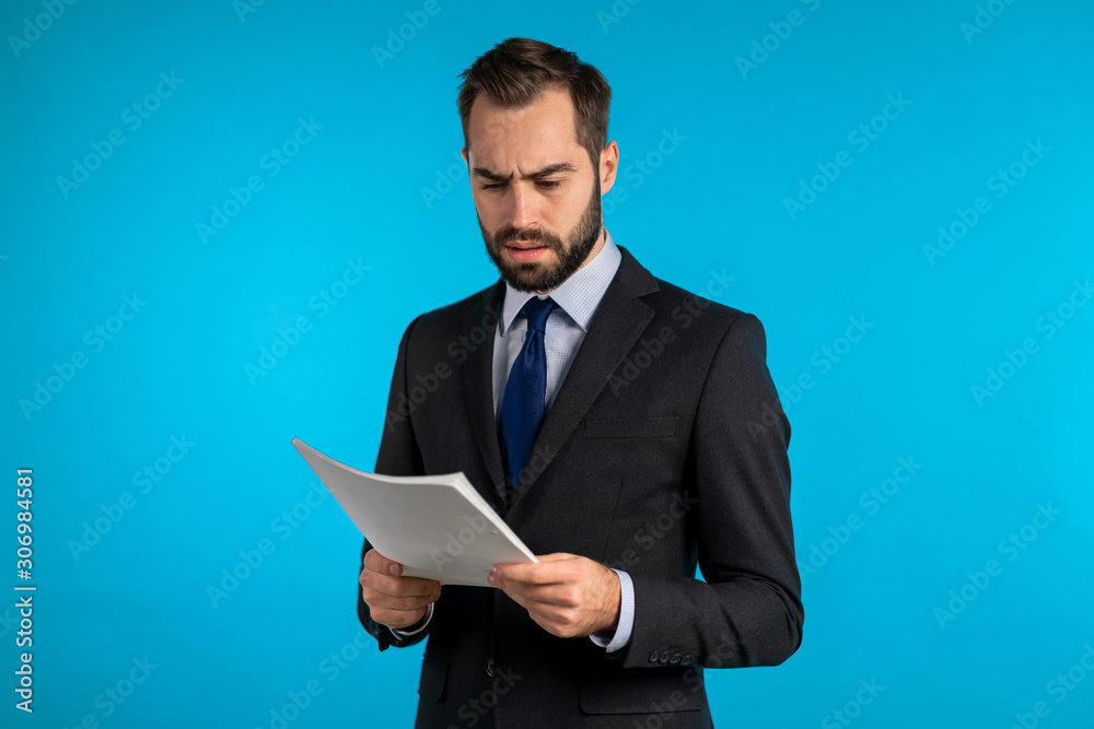 Serious businessman boss isolated on blue background studio. Man is unsatisfied with work of staff. Young mature male office employee in suit jacket with documents, reports or contract