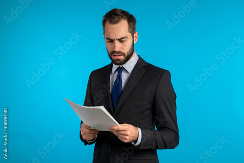 Serious businessman boss isolated on blue background studio. Man is unsatisfied with work of staff. Young mature male office employee in suit jacket with documents, reports or contract
