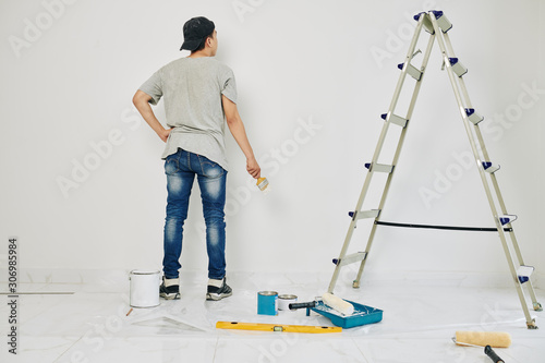 College student with brush painting wall in rented room in white color