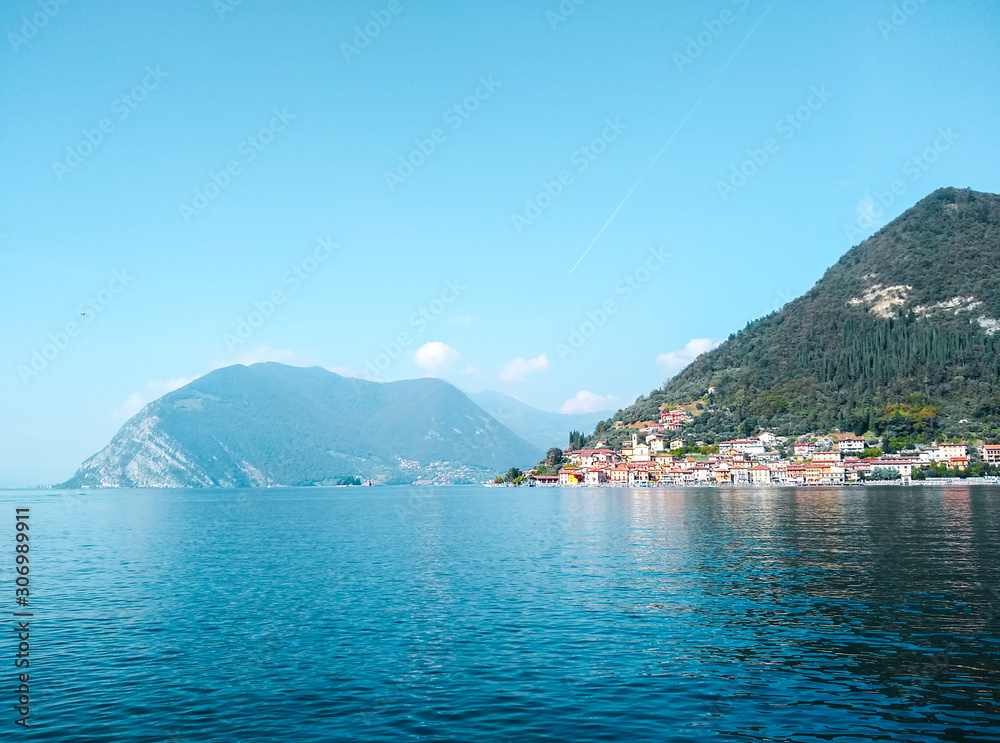 Sunny day on Lake Iseo (Lago d'Iseo) with the view of Monte Isola (Montisola), Peschiera Maraglio village. Blue sky and water. Italy, the Alps. Lombary region, Northern Italy.