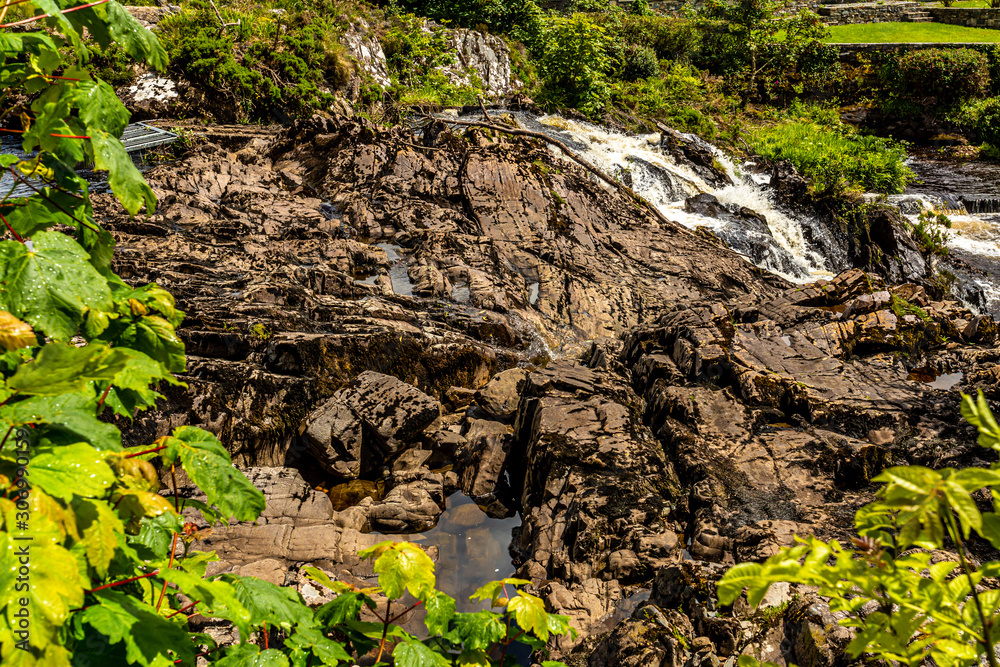 Water flow between limestone rocks at Clifden waterfalls on the Owenglin or Owenglen river among green vegetation, sunny spring day in the province of Connacht, Ireland Water flow between limestone rocks at Clifden waterfalls on the Owenglin or Owenglen river among green vegetation, sunny spring day in the province of Connacht, Ireland