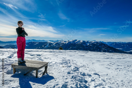 A girl in skiing outfit standing in a mountain pose on a bench, surrounded by powder snow in Bad Kleinkirchheim, Austria. Girl is practising yoga in the nature, finding inner peace and connection photo