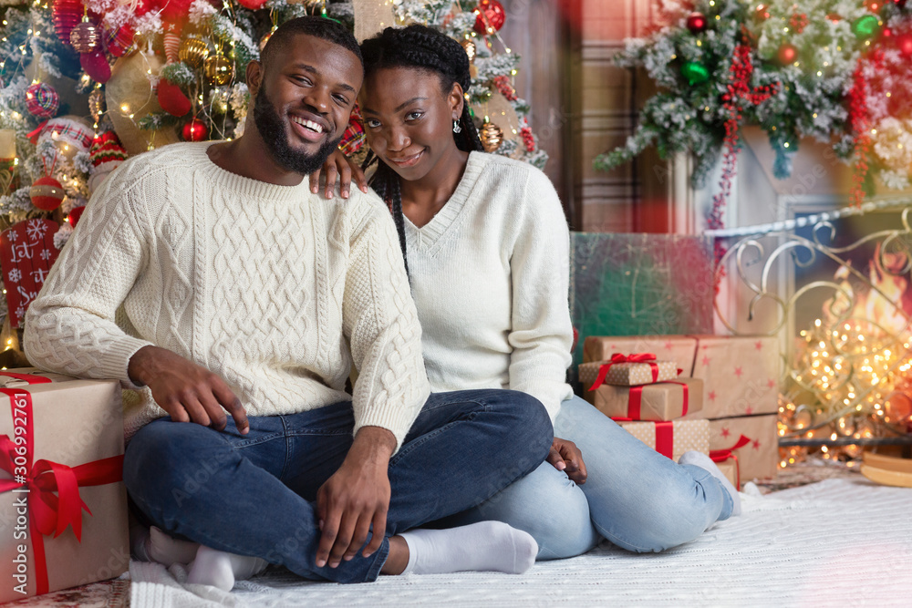 Portrait of romantic black couple sitting on floor near Xmas tree Portrait of romantic black couple sitting on floor near Xmas tree