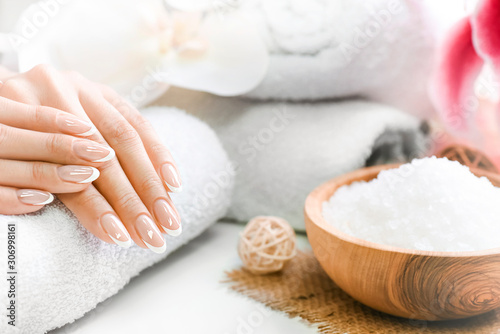Woman beautiful hands with precise french manicure. Nails care and spa treatment or procedure. Relaxing concept with salt in olive bowl.