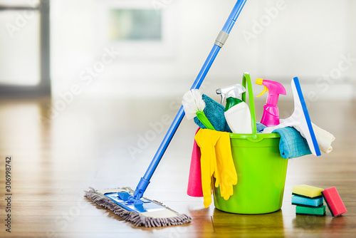 Bucket with cleaning items on blurry modern kitchen background. Washing brush and spray set with copy space.