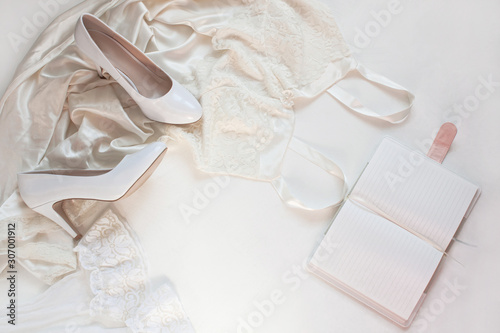 Wedding flat lay, womans stylish fashion accessories in biege colors on white background,copy space. Bridal details concept, silk lace dress, notebook mockup, fashion shoes,trendy composition,top view
