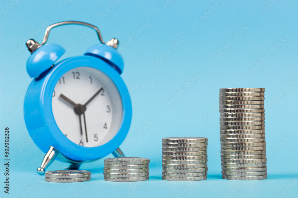 copy spaсe, stacked coins one on one in ascending order on the background of the alarm clock, blue background copy spaсe, stacked coins one on one in ascending order on the background of the alarm clock, blue background