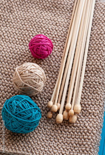 Colorful balls and wooden needles lying on beige knitted background