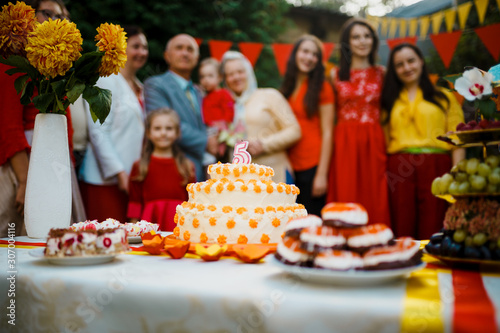 Family celebration birthday baby outside in the backyard.Big garden party. Selective focus on the cake with a candle 5 years old  blurred people big family on the background