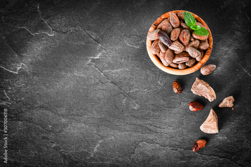 Raw cocoa beans with mint on dark stone table top view, black background. copy space for text. Panorama or banner concept. Raw cocoa beans with mint on dark stone table top view, black background. copy space for text. Panorama or banner concept.