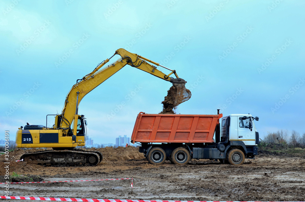 Excavator load the sand to the heavy dump truck on construction site. Excavators and dozers digs the ground for the foundation and construction of a new building. Apartment renovation program Excavator load the sand to the heavy dump truck on construction site. Excavators and dozers digs the ground for the foundation and construction of a new building. Apartment renovation program