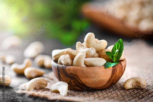 Cashew nuts in wooden bowl on dark black table with mint leaf on top. Raw cashews side view. photo