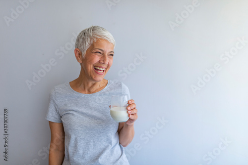 Cheerful mature woman having fun while drinking milk. Senior woman drinking from a clear glass full of milk. Woman in her golden age. Smiling, beautiful senior lady drinking a glass of milk photo