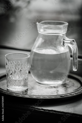 Jug of water and a glass on the windowsill, black and white photo.