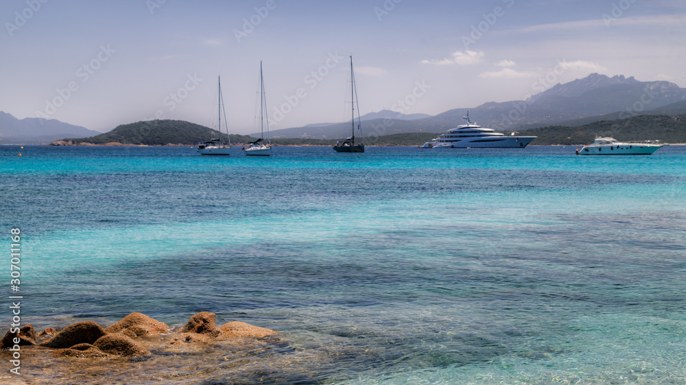 Sardinia, Italy, holidays. Sea with crystal clear azure water, yachts and ships in the sea, mountains in the background.