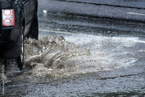 Car splashes through large puddle on flooded street. Motion car  rain  big puddle of water spray from wheels