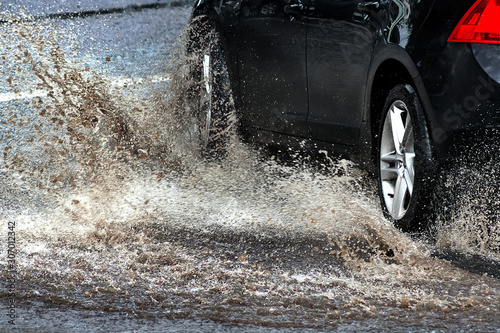 Car splashes through large puddle on flooded street. Motion car, rain, big puddle of water spray from wheels