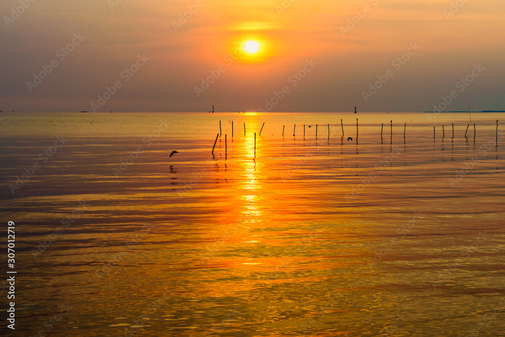 Beautiful nature landscape bright yellow sun reflecting orange light on the water surface of the sea and golden sunlight in sky, Colorful sunset at the tropical coast in Bangpu, Samut Prakan, Thailand