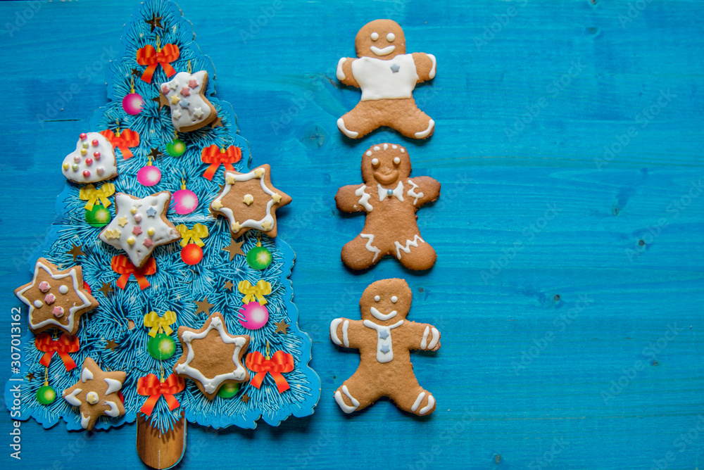 Christmas homemade gingerbread man cookies, on blue wooden background with decorated blue Christmas tree. Greeting card concept