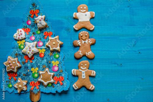 Christmas homemade gingerbread man cookies, on blue wooden background with decorated blue Christmas tree. Greeting card concept