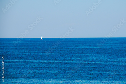 White sailboat on blue ocean horizon with blue sky © Janice Higgins