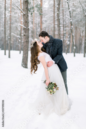 Winter wedding. Beautiful young couple, embracing and kissing in the winter snowy forest. © sofiko14