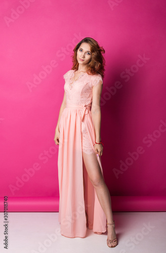 Slim pretty redhead woman in pink dress over studio background