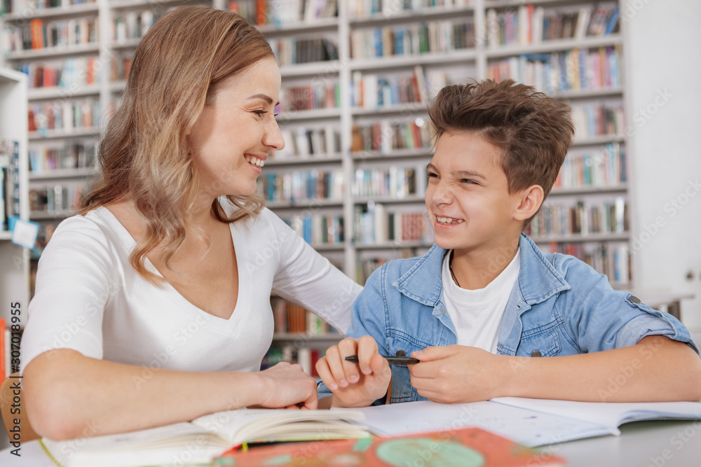 Lovely young woman talking to her cute little son while doing school assignment at the library Lovely young woman talking to her cute little son while doing school assignment at the library
