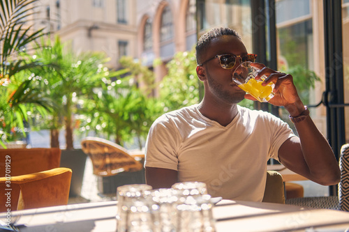 American student is drinking fruit juice at cafe on hot sunny day.