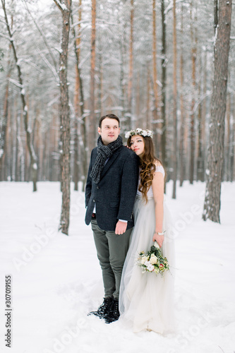 Winter wedding couple, bride and groom hugging in the snowy forest at their wedding day