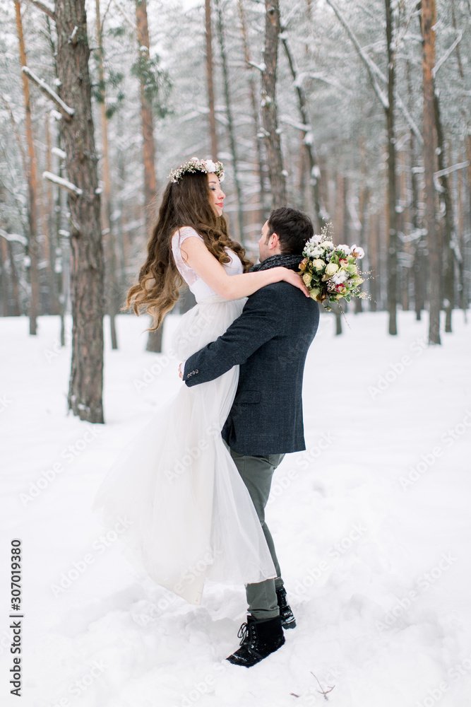 Happy wedding couple outdoors on winter day, handsome groom is holding her bride on the hands Happy wedding couple outdoors on winter day, handsome groom is holding her bride on the hands