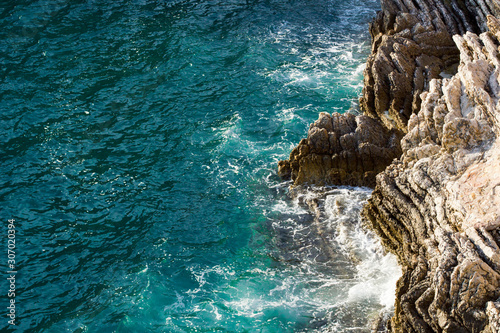 Waves crashing on rocky cliff with white spray and foam on deep blue sea water.