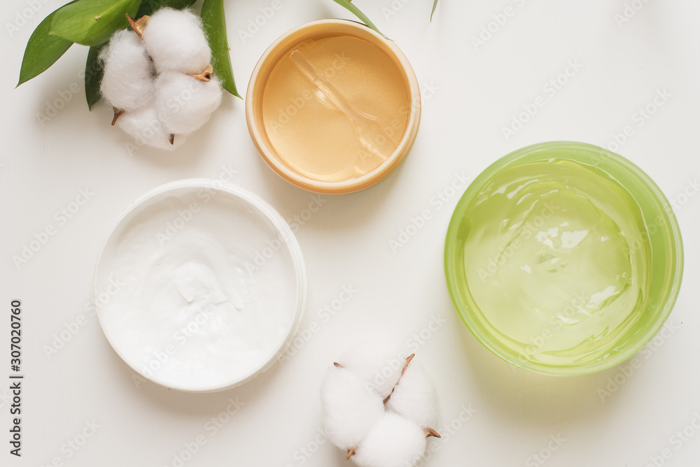 Jars of cream, aloe gel and moisturizing face patches on a white background next to cotton flowers. Nature Cosmetics for hand and face skin care, a means to reduce wrinkles on hands, moisturizing Jars of cream, aloe gel and moisturizing face patches on a white background next to cotton flowers. Nature Cosmetics for hand and face skin care, a means to reduce wrinkles on hands, moisturizing